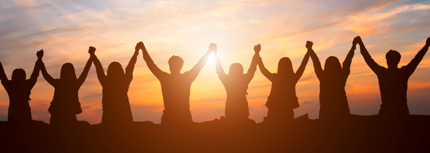 Eine Gruppe von Menschen steht im Sonnenuntergang nebeneinander und hält sich an den Händen hoch