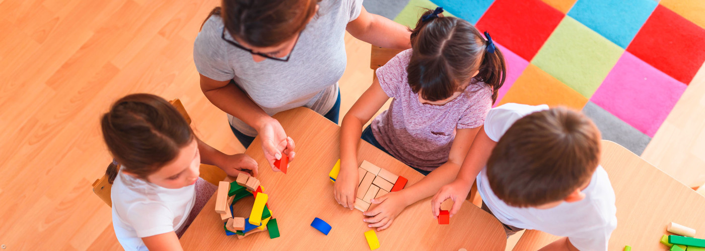 Mehrere Kinder sitzen an einem Tisch und spielen mit bunten Holzbausteinen.