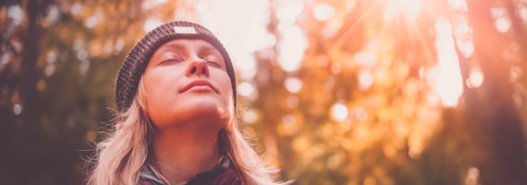 Eine Frau mit langem, blondem Haar und schwarzer Strickmütze im Wald.