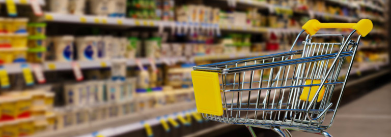 Leerer Einkaufswagen mit gelben Griffen vor Regalen in einem Supermarkt