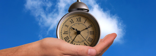 Eine Hand hält eine runde Taschenuhr mit römischen Ziffern vor blauem Himmel in die Höhe.