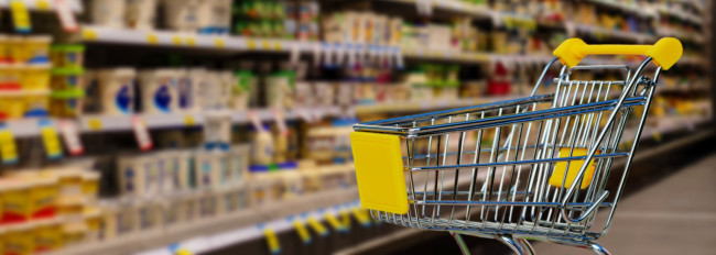 Leerer Einkaufswagen mit gelben Griffen vor Regalen in einem Supermarkt