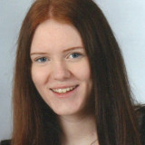 Frau Heim mit langen, glatten, rotbraunen Haaren vor hellem Hintergrund