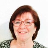 Frau Loch mit kurzen rotbraunen Haaren, trägt ein schwarzes Oberteil mit weißem Blumenmuster und kleinen silbernen Ohrringen