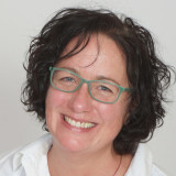 Frau Walther mit schulterlangem, lockigem dunklem Haar, trägt weiße Bluse